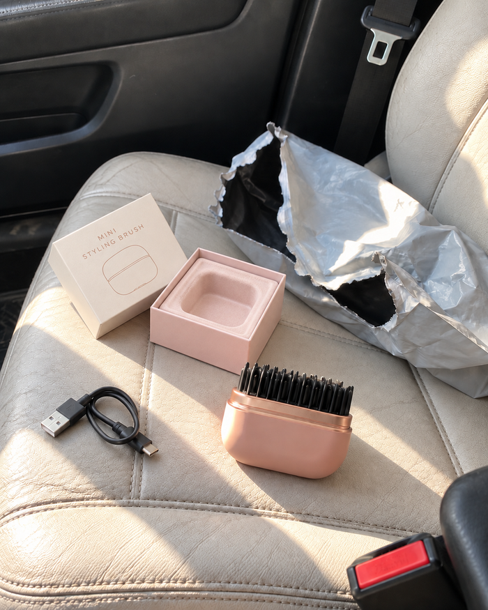 Jenny's rose pink mini styling brush, USB charging cable and opened packaging on a car seat